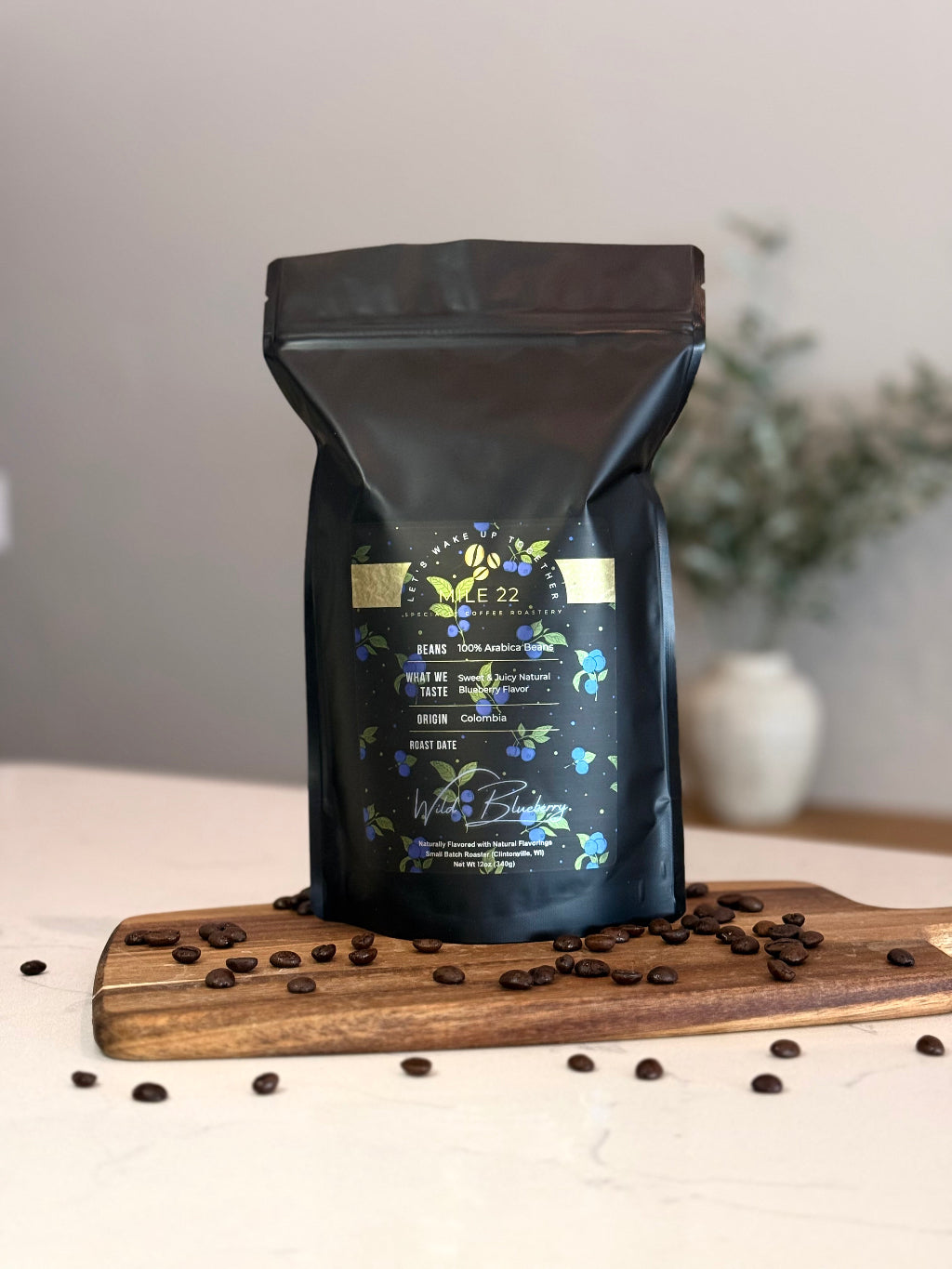 Black coffee bag with branding on a wooden board with scattered coffee beans
